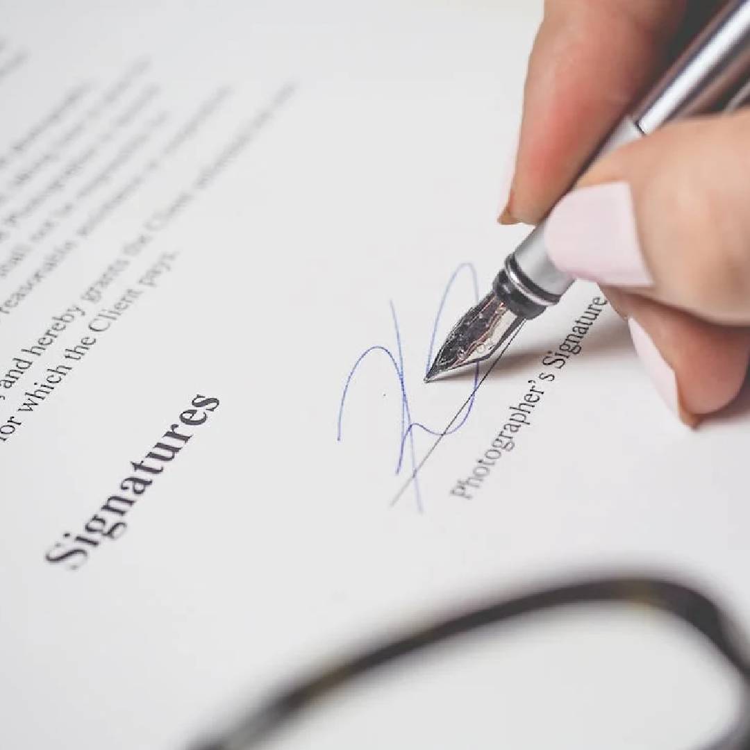 A person signing papers with a pen and scissors.