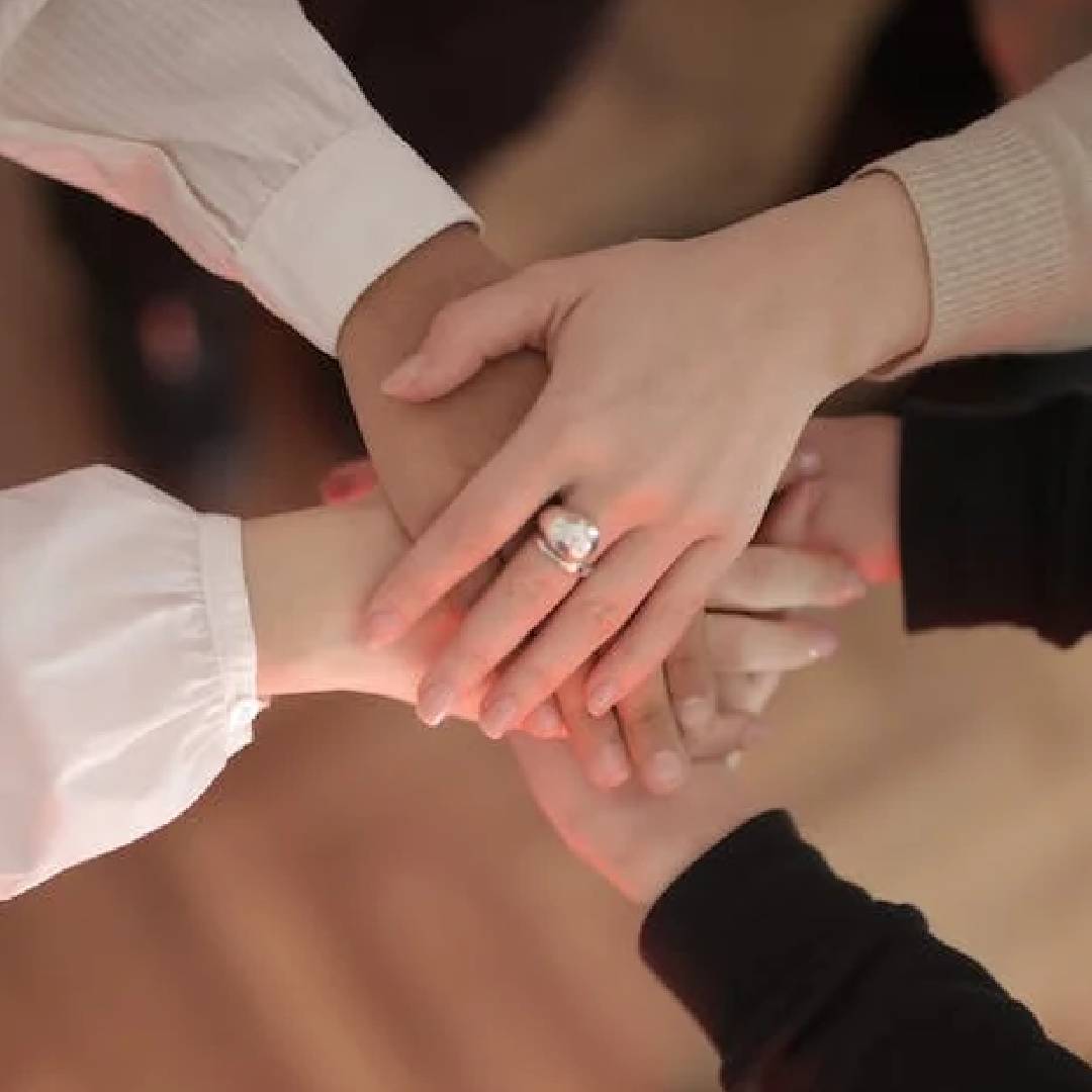 A group of people holding hands with one person wearing an engagement ring.