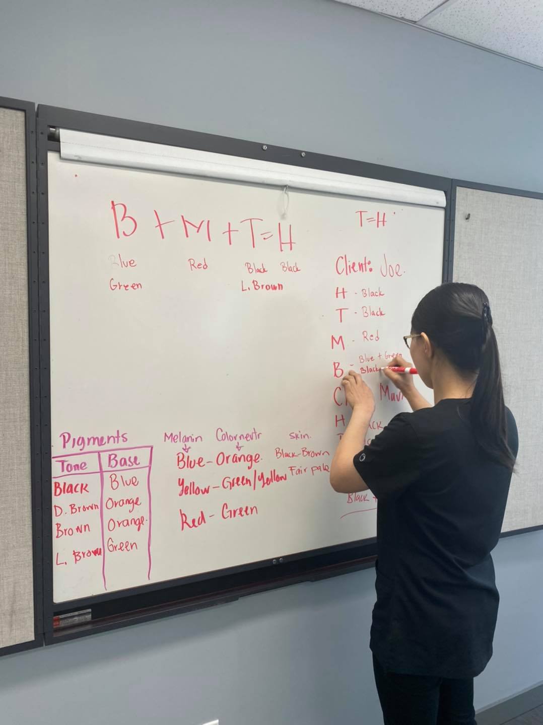 A woman writing on a white board with red ink.