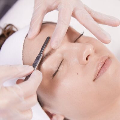 A woman getting her eyebrows trimmed by an esthetician.