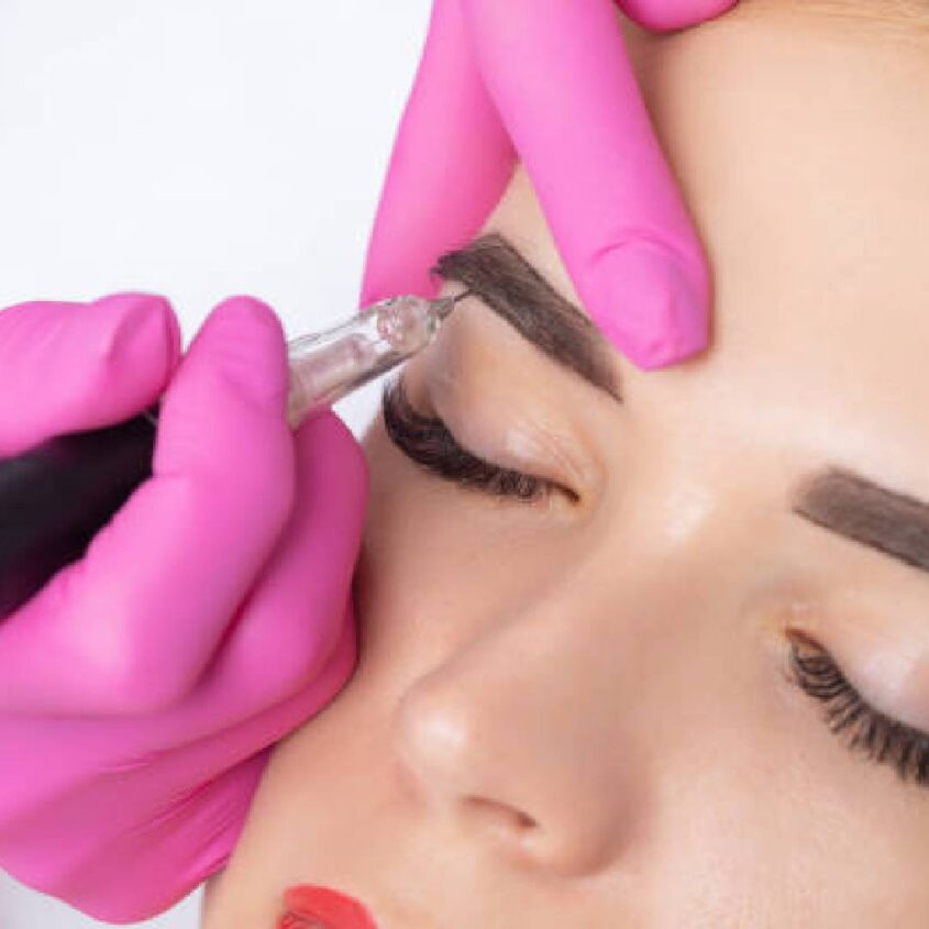 A woman getting her eyebrows tattooed by an esthetician.