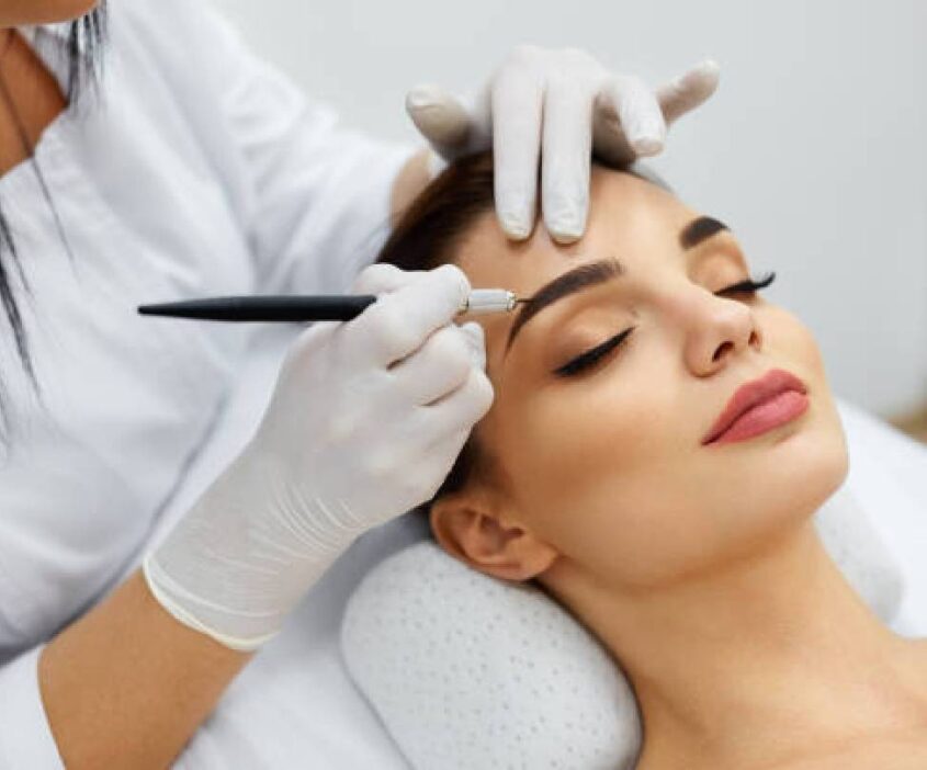 A woman getting her eyebrows tattooed by an esthetician.